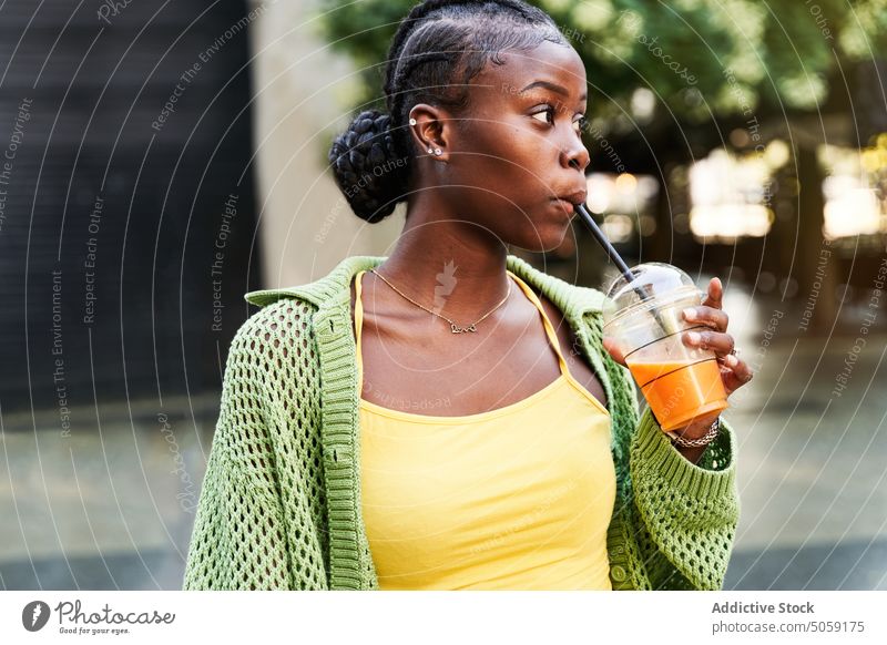 Junge schwarze Frau trinkt Saft und lächelt im Park trinken Imbissbude Stil selbstbewusst Erfrischung zum Mitnehmen jung Afroamerikaner ethnisch Geflecht Straße