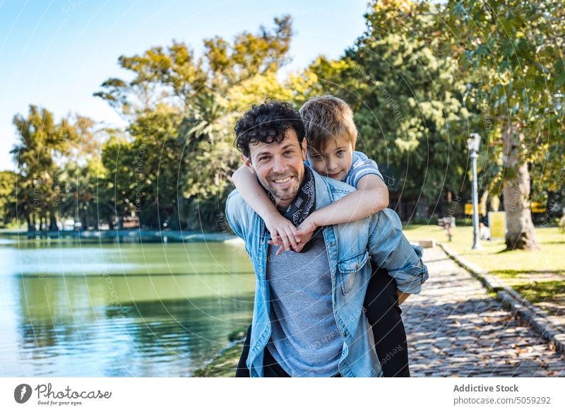 Vater mit Sohn in der Nähe des Sees im Park Huckepack Mitfahrgelegenheit Lächeln Herbst Wochenende Zusammensein Mann Junge Glück Liebe Weg Kindheit froh führen