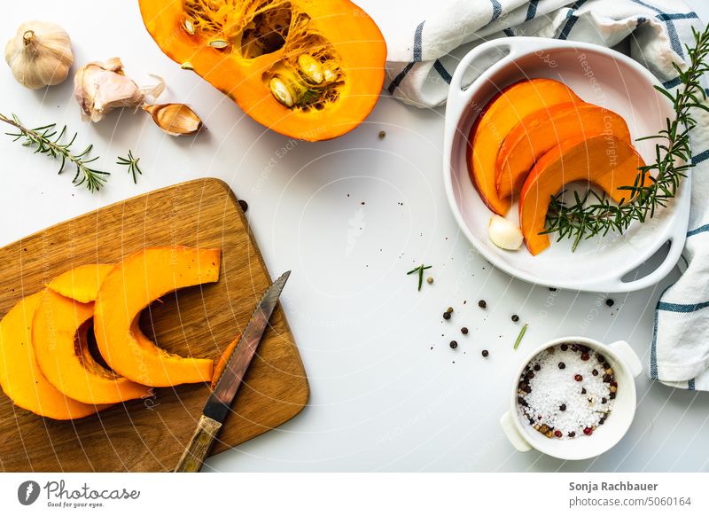 Hokkaido Kürbis in Scheiben auf einem Schneidebrett und Zutaten auf einem weißen Tisch hokkaido Gemüse Herbst Bioprodukte roh Lebensmittel orange frisch