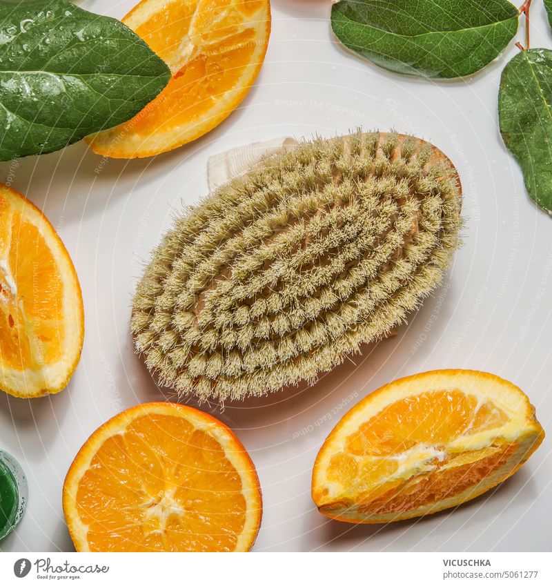 Körperpflege Massagebürste und orange Früchte Scheiben mit grünen Blättern auf weißem Hintergrund, Ansicht von oben orangefarbene Früchte grüne Blätter