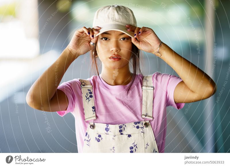 Stilvolle asiatische Frau passt den Hut an Hut anfassen ausrichten Verschlussdeckel urban Straße Vorschein lässig Porträt jung ethnisch Individualität
