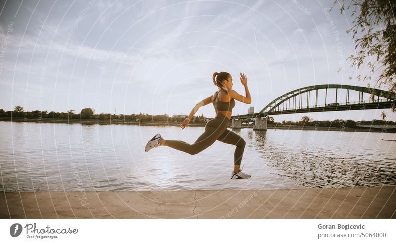 Aktive junge schöne Frau läuft auf der Promenade am Flussufer entlang aktiv Aktivität Athlet sportlich Großstadt Ausdauer Übung Fitness Gesundheit Jogger Joggen