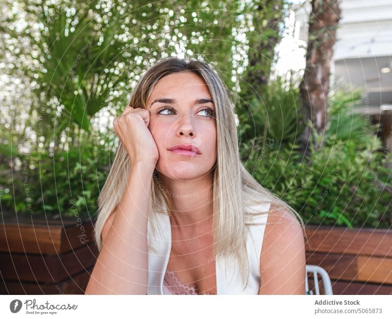 Nachdenkliche Frau sitzt auf der Terrasse sich auf die Hand lehnen Denken Sommer blond nachdenklich gelangweilt Wochenende tagsüber jung Erwachsener nachdenken