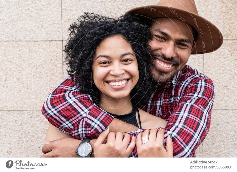 Glückliches hispanisches Paar, das sich in der Nähe der Wand umarmt Umarmung Straße Liebe Zusammensein Partnerschaft Lächeln Porträt tagsüber froh Zuneigung
