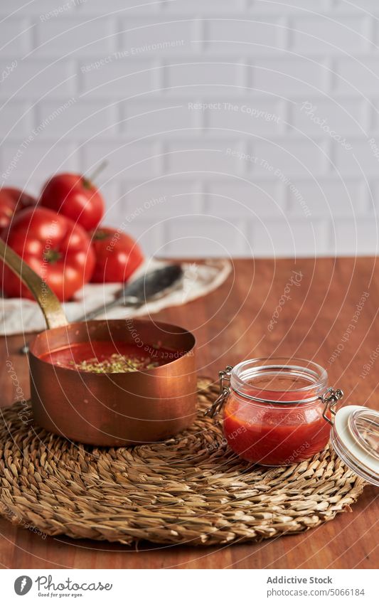 Behälter und Pfanne mit Tomatensauce auf dem Tisch Saucen Container Zusammensetzung selbstgemacht gewebt Unterlage Küche heimwärts Kochtopf Glas