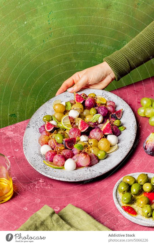 Anonyme Person mit Weintrauben und Olivensalat Küche Vegetarier Tisch Käse Salatbeilage Rezept Trauben oliv Mozzarella Blätter frisch Zutaten Lebensmittel