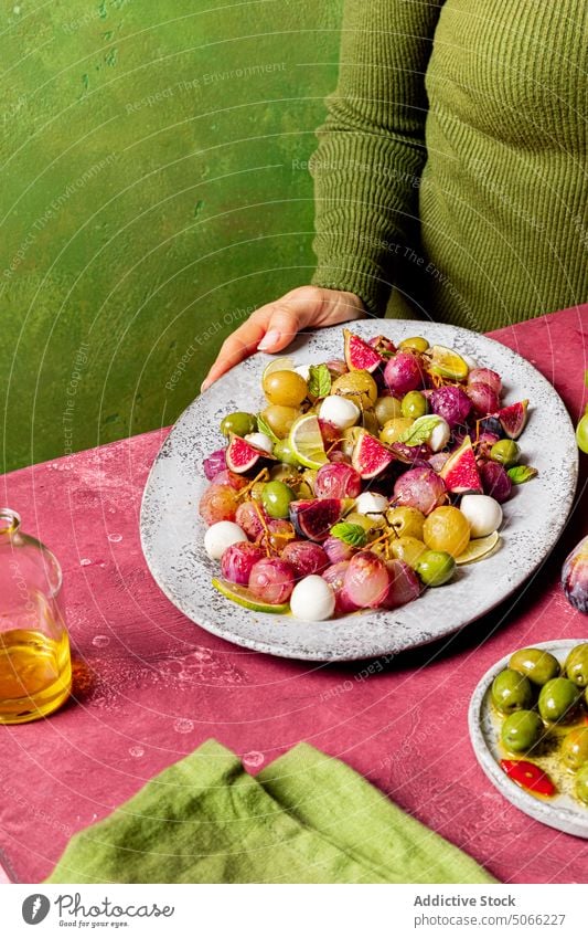 Anonyme Person mit Weintrauben und Olivensalat Küche Vegetarier Tisch Käse Salatbeilage Rezept Trauben oliv Mozzarella Blätter frisch Zutaten Lebensmittel