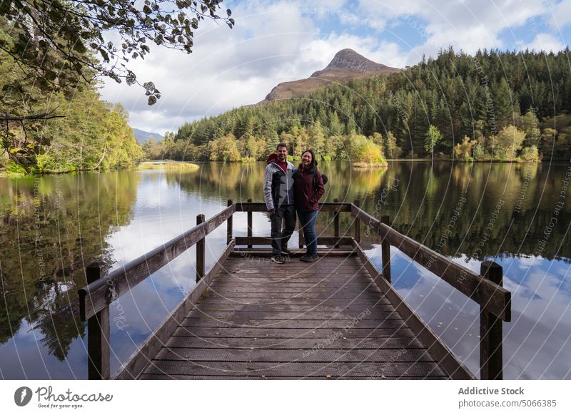 Verschiedenes Paar am Kai in der Nähe des Sees Pier Berge u. Gebirge Wald Umarmung Zusammensein Reisender Lächeln Glück Glencoe-Lochan Schottland Großbritannien