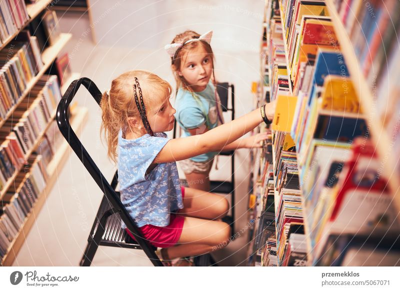 Schülerinnen suchen in der Schulbibliothek nach Büchern. Schüler wählen bestimmte Bücher aus. Grundschulbildung. Erledigung der Hausaufgaben. Zurück zur Schule