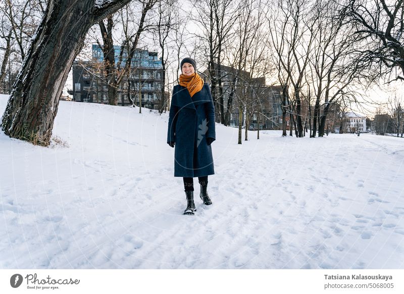 Eine fröhliche junge Frau geht durch eine winterliche Stadt Winter kalt Schnee Fröhlichkeit Glück Freude Menschen Person Erwachsener Mantel Lächeln jauchzen