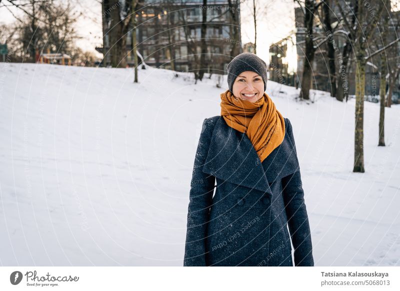 Lächelnde Frau in einem Wintermantel, Schal und Mütze vor dem Hintergrund einer verschneiten Stadt kalt Schnee Fröhlichkeit Glück Freude Menschen Person