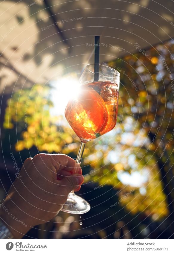 Crop-Person mit erfrischendem Schorle-Cocktail Sommer Sonnenuntergang Glas Aperol spritzen trinken Alkohol Resort Feiertag Weinglas Kälte Getränk Stroh