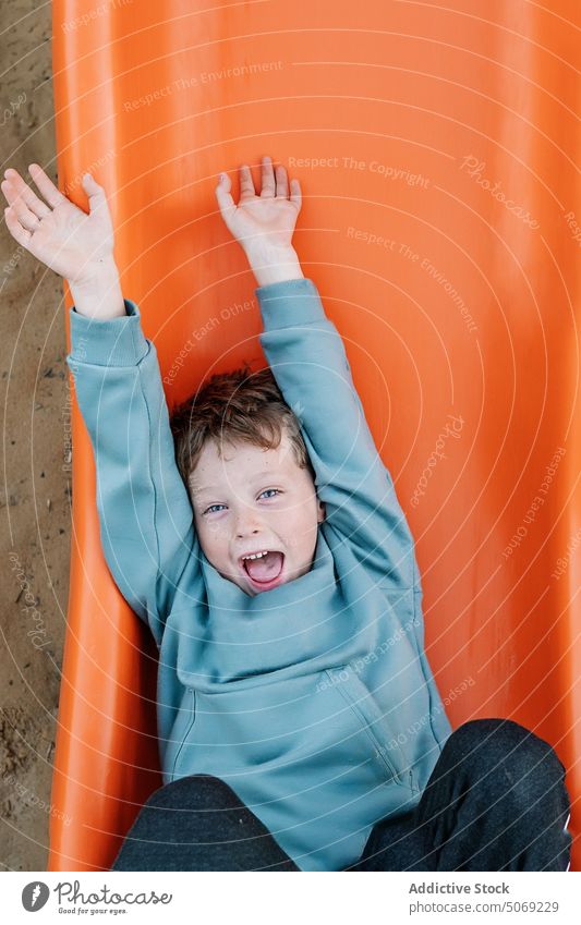 Fröhlicher Junge spielt auf orangefarbener Rutsche spielen Sliden Spielplatz Sand Barfuß zeigen dreckig Glück Wochenende Sommer Kind Boden Zeitvertreib