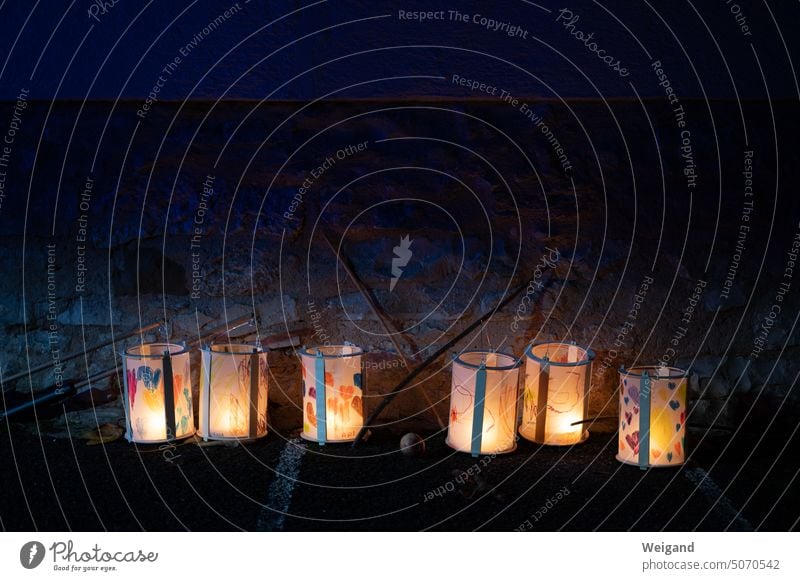 Leuchtende Laternen aus Papier für den St. Martinsumzug im November in einer Reihe auf dem Boden vor einer Steinmauer bei dunkler Nacht aufgestellt Licht