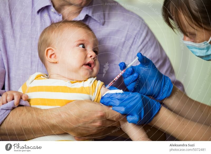 Weibliche Krankenschwester mit chirurgischer Maske und in Handschuhen gibt einem Baby in der Klinik eine Impfstoffinjektion. Impfung von Kleinkindern.