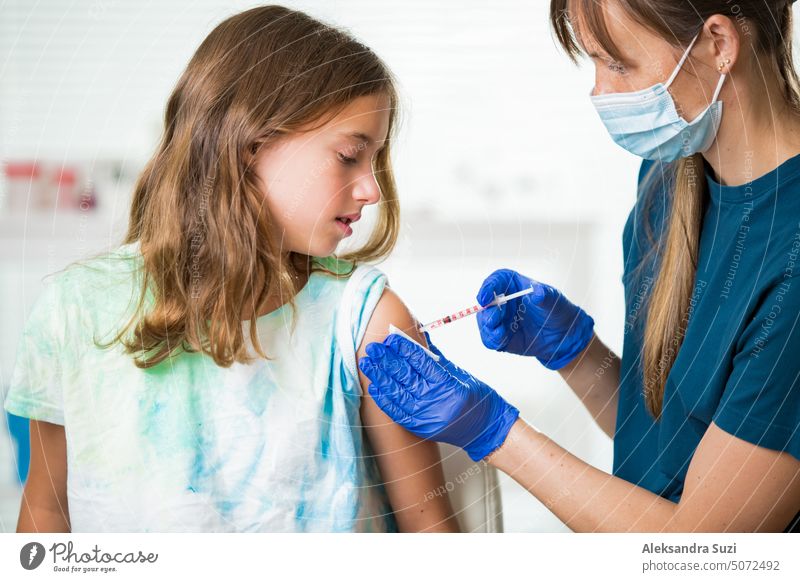 Weibliche Krankenschwester mit chirurgischer Maske und in Handschuhen gibt einem Teenager in der Klinik eine Impfstoffinjektion. Kinderimpfung. Antibiotikum