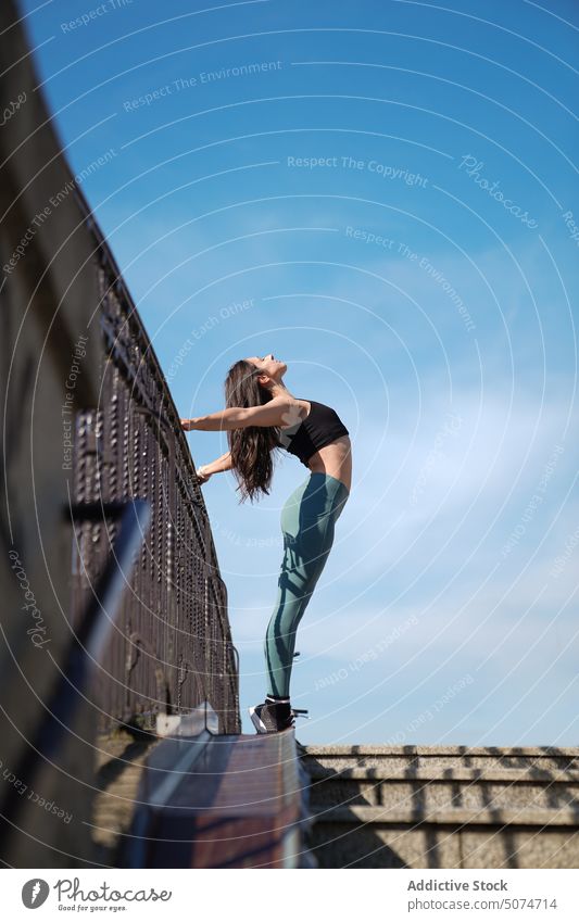 Sportliche Frau streckt ihren Körper und hält sich am Geländer fest Übung Dehnung beweglich Training Reling Treppenhaus Sportlerin Athlet sportlich passen