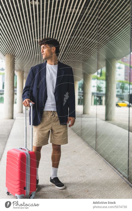 Junger Mann mit Koffer auf der Straße Lächeln Gebäude Flughafen Reisender Glaswand Ausflug Wochenende männlich jung smart lässig Gepäck Tourist Stil Tourismus