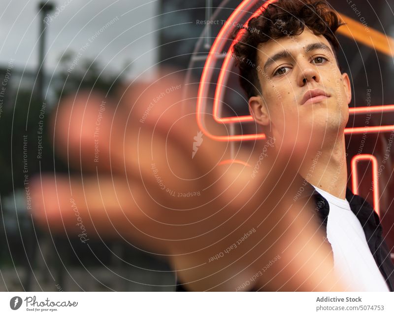 Junger Mann streckt die Hand zur Kamera aus sich[Akk] melden Straße urban Zeichen neonfarbig Glaswand Vorschein leuchten Stil männlich jung dunkles Haar