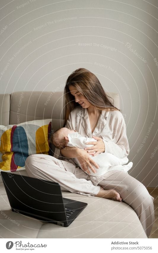 Mutter mit Baby am Laptop auf dem Sofa benutzend freiberuflich Umarmung Wohnzimmer heimwärts Projekt Frau jung Säugling neugeboren abgelegen Umarmen Internet