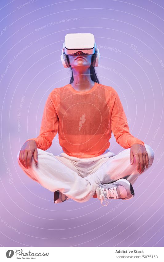 Frau meditiert in der virtuellen Realität meditieren VR Headset Windstille Yoga Lotus-Pose Konzept schweben futuristisch Beine gekreuzt Schutzbrille Vitalität