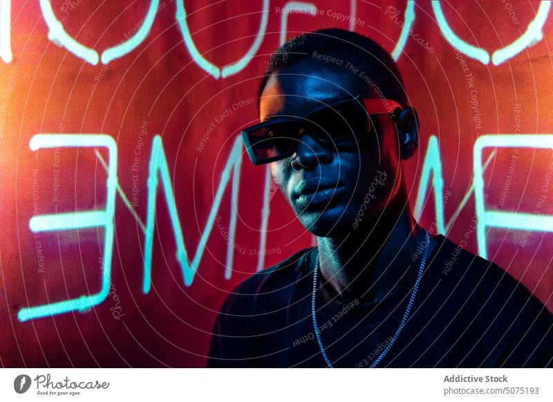 Cooler schwarzer Mann mit modischer Sonnenbrille im Neonlicht cool neonfarbig Mode Metaversum selbstbewusst ultraviolett Licht Nachtclub leuchtend männlich