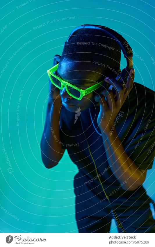 Schwarzer DJ mit Discobrille, der in einem Nachtclub den Ton über Kopfhörer überprüft Mann dj Schutzbrille Metaversum Klang prüfen zuhören Musik neonfarbig