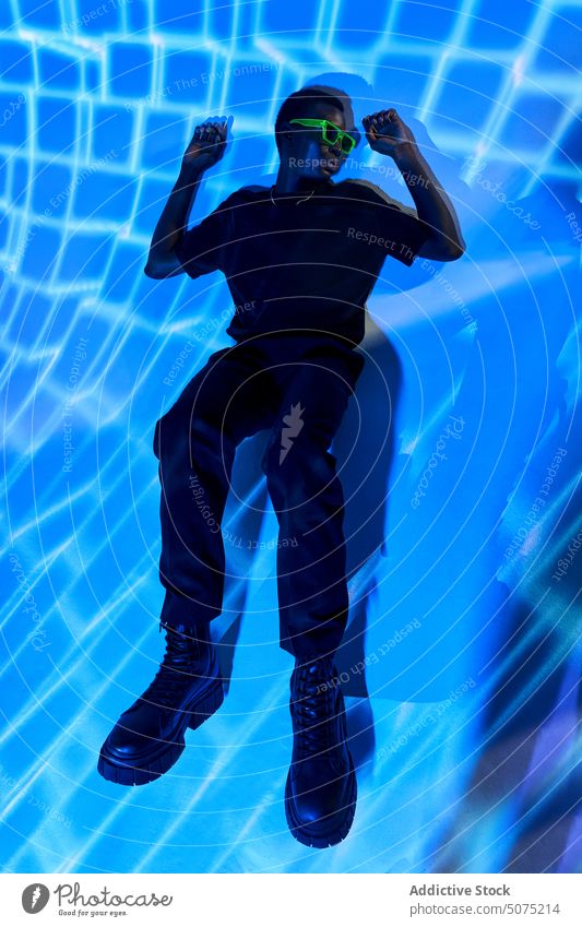 Außergewöhnlicher schlanker schwarzer Mann auf dem Boden liegend in geometrischem Neonlicht außergewöhnlich Lügen neonfarbig Licht ultraviolett Metaversum cool