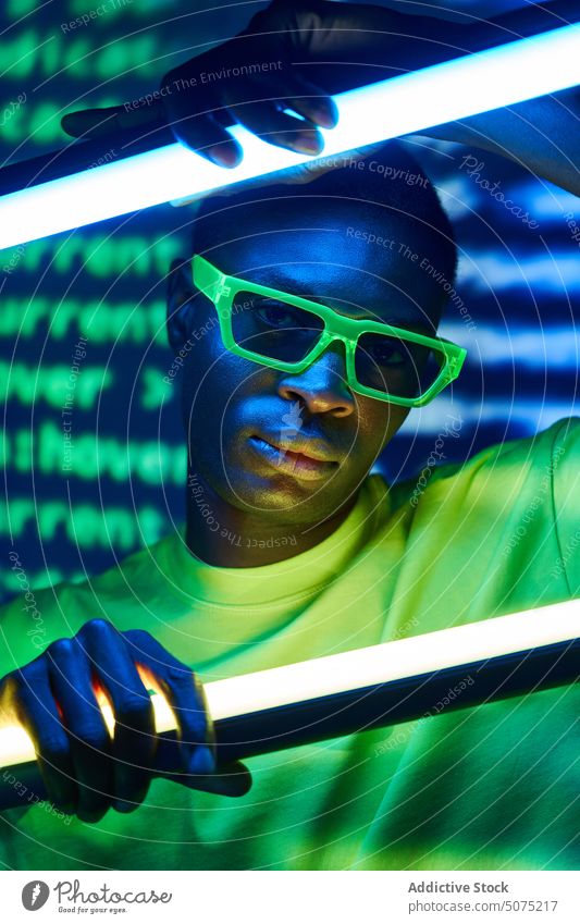Cooler trendiger schwarzer Mann mit Sonnenbrille, der Neonlampen in einem Disco-Club berührt cool trendy Metaversum emotionslos außergewöhnlich Mode