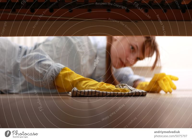Reinigung und Desinfektion von Oberflächen. Frau mit gelben Gummihandschuhen und Lappen reinigt Boden unter Bett. Schöne Frau putzt Haus. Hausreinigung Reinigen