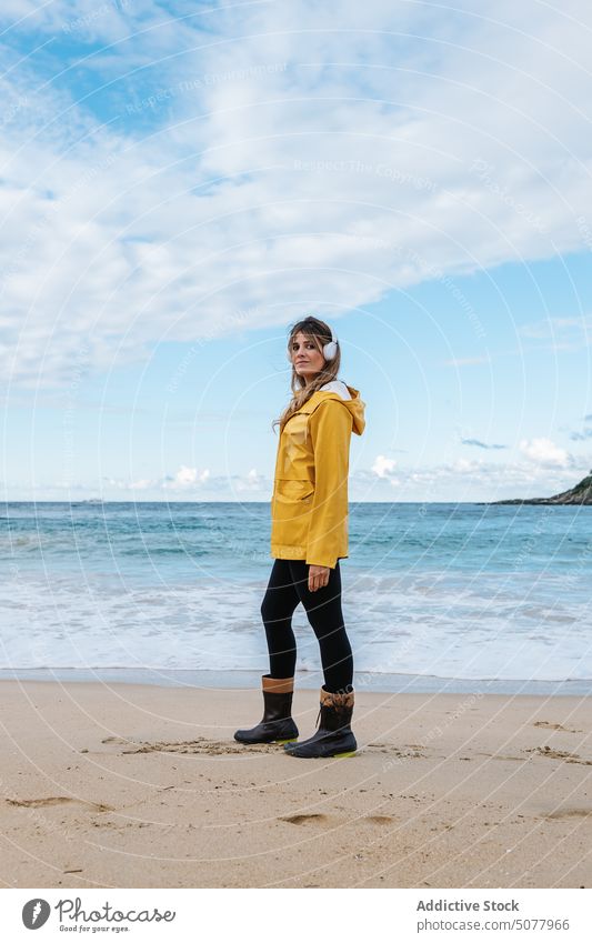 Frau mit drahtlosen Kopfhörern am Strand nachdenken warme Kleidung zuhören Gesang sich[Akk] entspannen sandig Küste wellig schäumen Meeresufer MEER