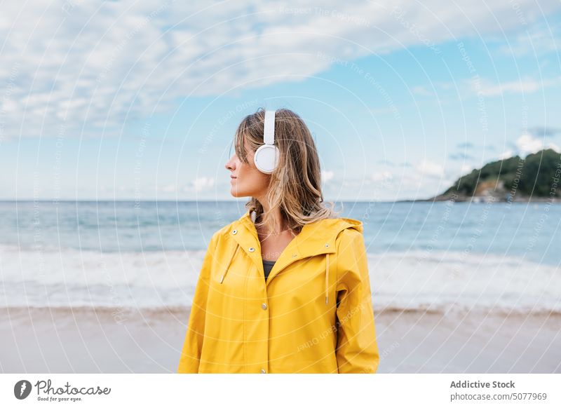 Frau mit kabellosen Kopfhörern, die über die Natur am Strand nachdenkt nachdenken warme Kleidung zuhören Gesang sich[Akk] entspannen sandig Küste wellig