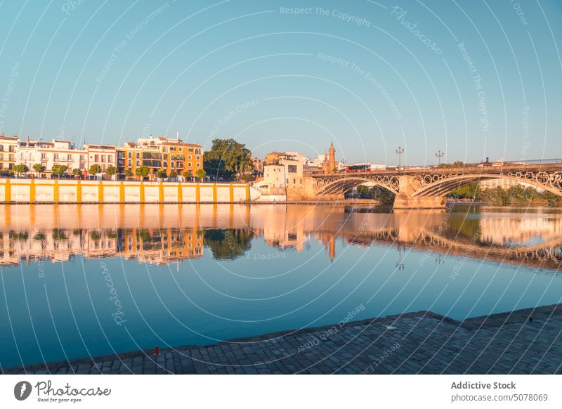 Alte Brücke über einen ruhigen Fluss mit einer Reihe von Gebäuden in Sevilla Außenseite gealtert Stauanlage friedlich historisch Spanien Architektur Andalusia