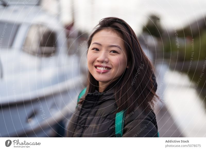Lächelnde asiatische Frau auf dem Pier stehend Kai Hafengebiet Porträt Kleintransporter Ausflug Rucksack Reise Urlaub Abenteuer Feiertag positiv aufgeregt Glück