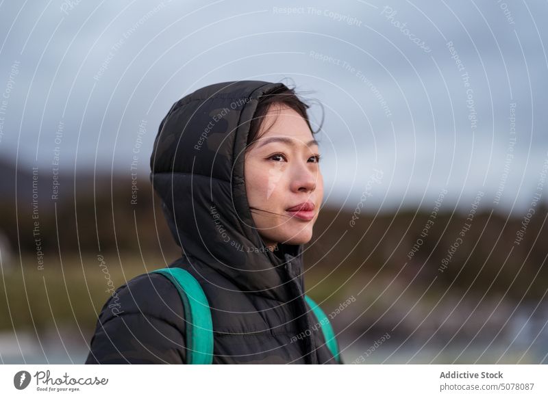 Verträumte asiatische Frau in warmer Kleidung steht draußen Reisender Wanderer Oberbekleidung Jacke Regen kalt Wetter Ausflug Wochenende nachdenklich positiv