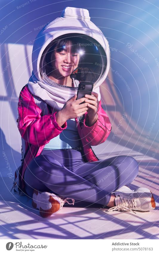 Glückliche asiatische Frau im Weltraumhelm mit Telefon Chinesisch futuristisch Smartphone Kosmonaut Schutzhelm Süchtige eintauchen Lächeln soziale Netzwerke