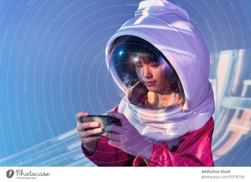 Asiatische Frau im Weltraumhelm beim Telefonieren Chinesisch futuristisch Smartphone Kosmonaut Schutzhelm Süchtige eintauchen soziale Netzwerke Konzept Raum