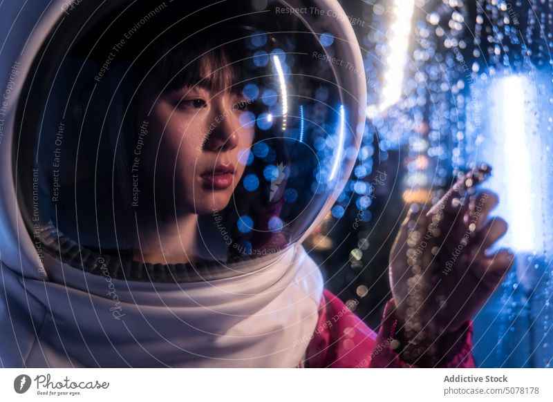 Chinesische Astronautin im Neonlicht Frau Schutzhelm Metaversum träumen behüten nachdenken Kosmonaut Raumanzug Konzept Tierhaut Windstille emotionslos