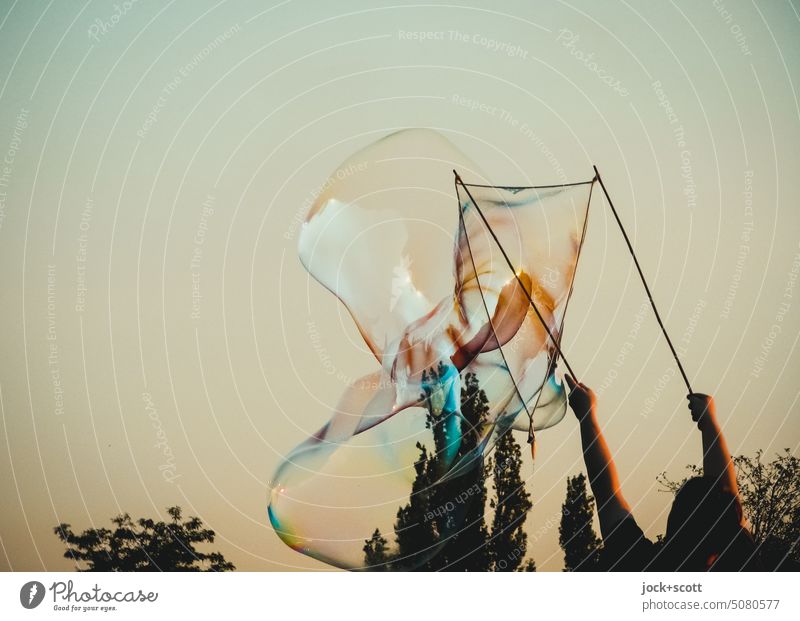 ein Seifenblasenkünstler mit einer Riesenseifenblase glänzend Schweben Leichtigkeit durchsichtig Stimmungsbild Transformation Hintergrund neutral