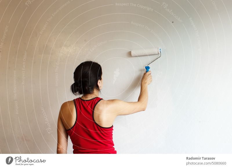 Frau streicht eine Wand mit einer Walze Malerei Rolle weiß im Innenbereich Renovierung Haus Farbe Person Verbesserung Arbeit Erwachsener jung heimwärts
