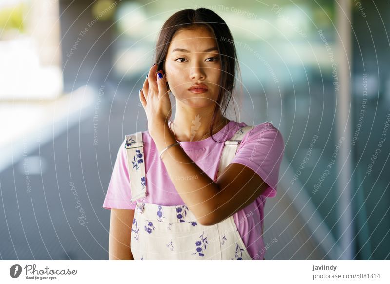 Junge asiatische Frau berührt Haare Haare berühren Straße Stil ausrichten Vorschein dunkles Haar urban tagsüber Porträt jung ethnisch lässig modern allein
