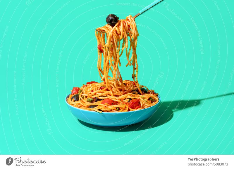 Spaghetti puttanesca aus einer Schüssel essen, minimalistisch auf grünem Hintergrund blau Schalen & Schüsseln hell Kapriolen Kohlenhydrate Nahaufnahme Farbe