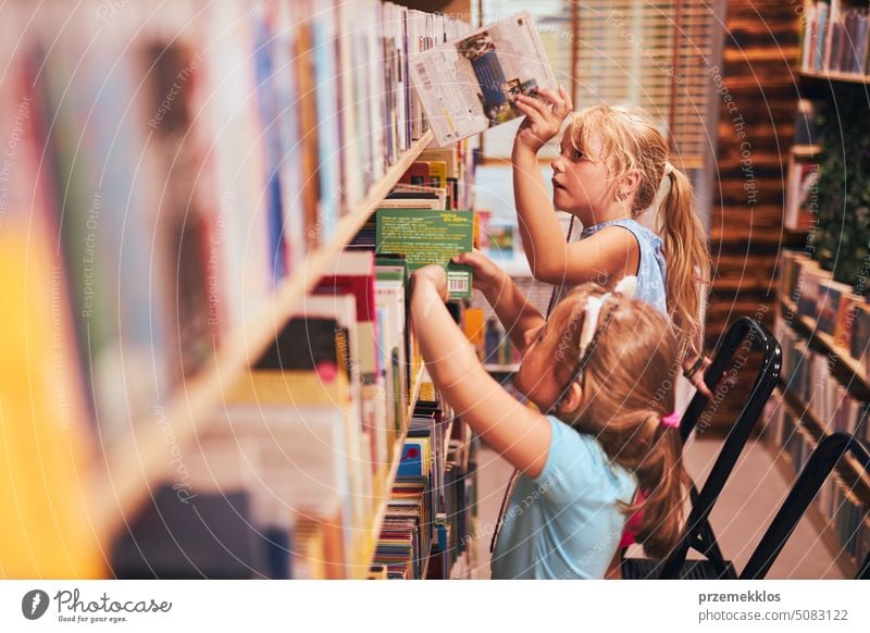 Schülerinnen suchen in der Schulbibliothek nach Büchern. Schüler wählen bestimmte Bücher aus. Grundschulbildung. Erledigung der Hausaufgaben. Zurück zur Schule
