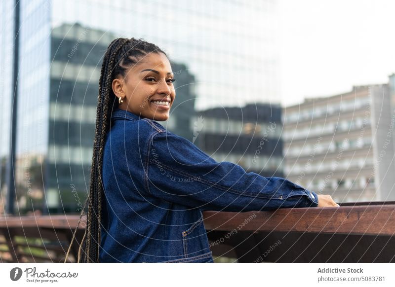 Fröhliche schwarze Frau steht auf einer Brücke gegen den Stadtverkehr Reling Stadtbild Verkehr Gebäude urban Kälte Straße Lächeln positiv Glück Afroamerikaner