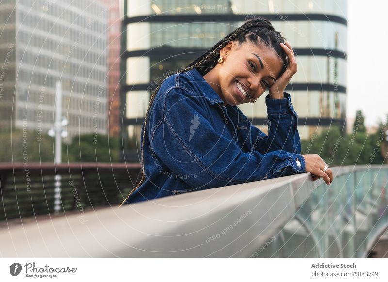 Fröhliche schwarze Frau steht auf einer Brücke gegen den Stadtverkehr Reling Stadtbild Verkehr Gebäude urban Kälte Straße Lächeln positiv Glück Afroamerikaner