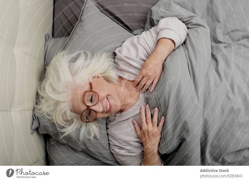 Ältere Frau mit Brille auf dem Bett liegend besinnlich nachdenklich Rentnerin Decke Bettwäsche Komfort ruhen Schlafzimmer sich[Akk] entspannen heimwärts Senior