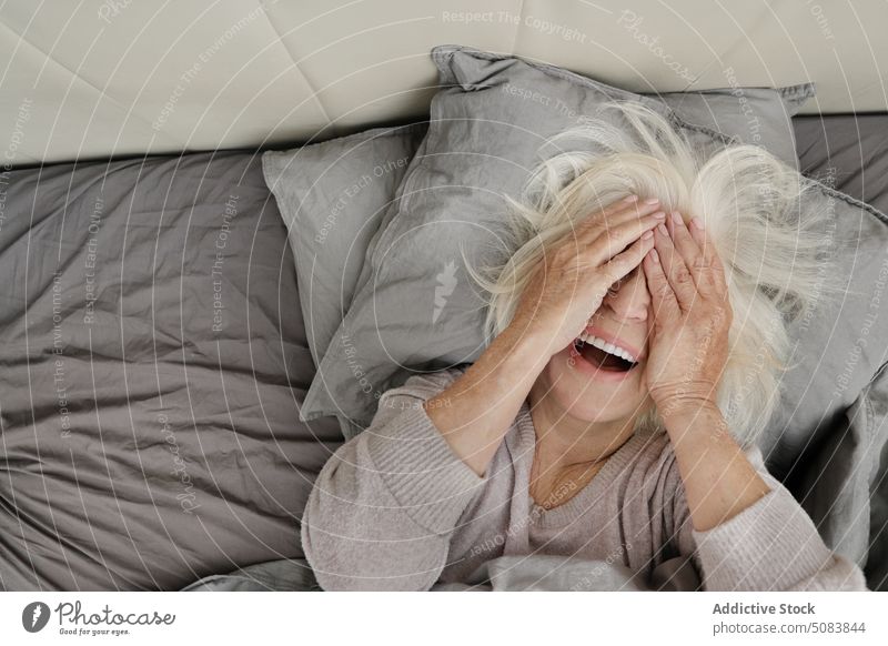 Ältere Frau liegt auf dem Bett und bedeckt ihr Gesicht Rentnerin Deckblatt Komfort ruhen Schlafzimmer Tierhaut Pullover Kopfkissen heimwärts älter