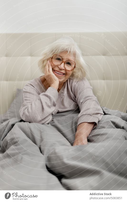 Ältere Frau mit Brille sitzt auf dem Bett Glück Rentnerin Decke Bettwäsche Komfort ruhen Schlafzimmer sich[Akk] entspannen heimwärts Senior Pullover weich Kälte