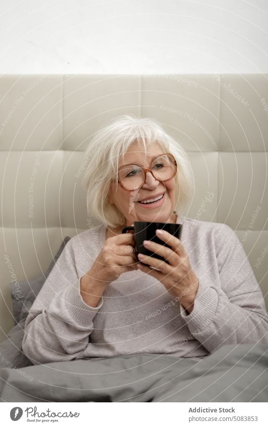 Positive ältere Frau trinkt Kaffee im Bett Lächeln trinken Morgen Schlafzimmer Becher Komfort Getränk Glück ruhen heimwärts Senior Tasse genießen