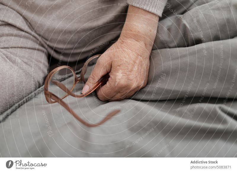Crop ältere Frau mit Brille auf dem Bett liegend Schlafzimmer heimwärts Decke Bettwäsche Komfort ruhen Senior sich[Akk] entspannen Rentnerin Pullover gealtert